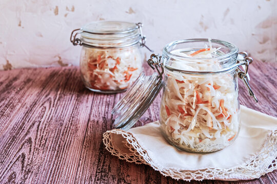 Two glass jars filled with homemade sauerkraut with carrots on wooden table. Fermented vegetables. Vegetarian vegan food. Fermented cabbage, german and russian style cuisine. Copy space.