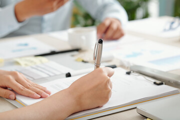 Close-up image of female entrepreneur singing agreement at meeting with business partner