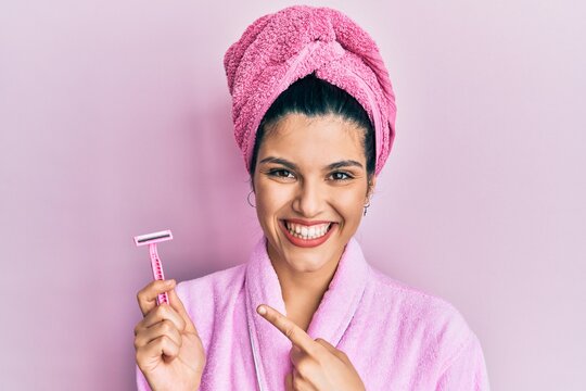 Young hispanic woman wearing shower bathrobe holding razor smiling happy pointing with hand and finger