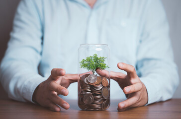 Businessman protect Tree which growth inside saving coins jar , Save money for investment and dividends from profit concept.