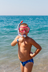 Tanned boy in a swimming mask stands by the sea