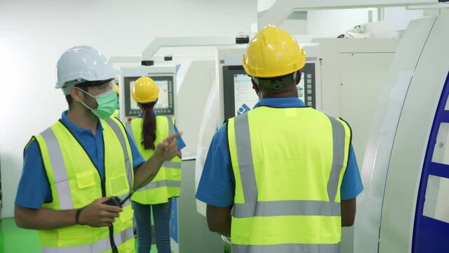 Caucasian male supervisor wear face mask checking Asian and Africa workers in factory production line. Concept of new normal working in Covid-19 pandemic and diversity.