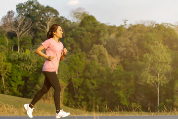 Sporty young woman running or jogging on the roadside in nature. Healthy lifestyle concept.