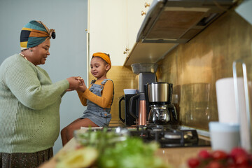 Side view portrait of cute African-American girl sitting on kitchen counter and enjoying healthy...