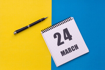 March 24th. Day 24 of month, calendar date. A notebook with a spiral and a pen lies on a yellow-blue background, flat lay, copy space