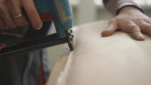 A man works in an upholstered furniture repair shop and attaches fabric to a wooden frame with a pneumatic stapler