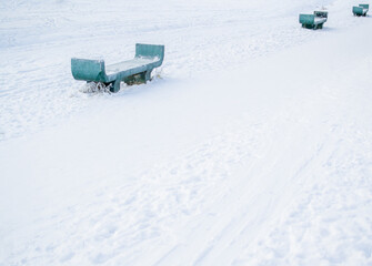 Green turquoise stone empty benches in a snowy winter park. Three seats. Footprints in the snow