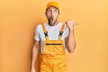 Young handsome man wearing handyman uniform over yellow background surprised pointing with hand...