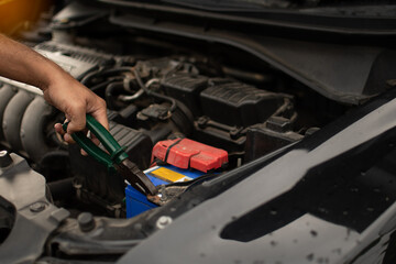 Closeup, The hands of a male technician are using a tool to replace the car battery, parked at home. Black car, the battery is damaged. Tools have pliers and screwdrivers.