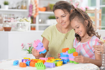 Young mother and little daughter playing blocks game