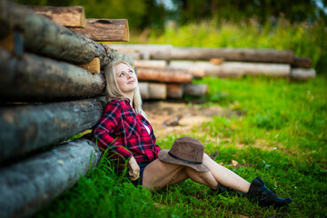 Young blonde woman dressed as a cowboy at a wooden fence at sunset, selective focus