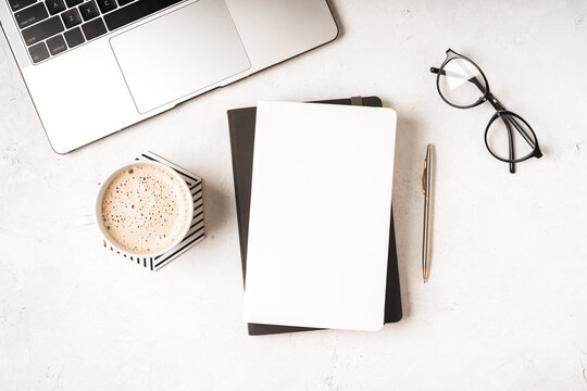 Top view blank paper Notebook, leaf, laptop keyboard, cup of coffee, glasses and pen. Desktop mock up, Flat lay of white working table background with office equipment, mockup.