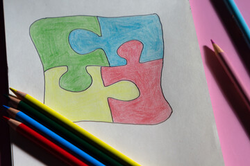 Autism awareness day or month. The drawn puzzle is colored in different colors as a symbol of autism awareness. Sketchbook and pencils for children's creativity.