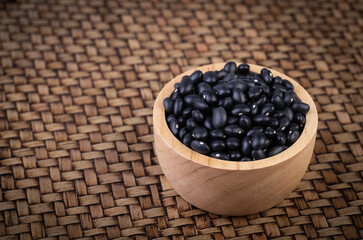 Black beans in a wooden cup placed on a bamboo weave.