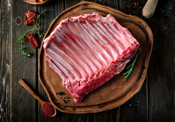 Raw lamb meat on the bone in a large whole piece, organic mutton with seasonings on a wooden...