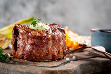 Big grilled Filet Mignon steak with butter and thyme served on a wooden board. Roast meat dish