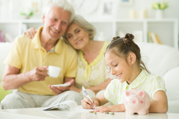 Obraz na płótnie Canvas Happy grandparents and grandchild with piggy bank at home