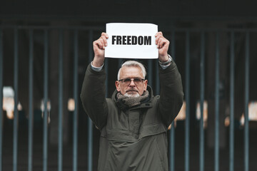 Protest for freedom against the background of the bars. An elderly man holds a poster with the...