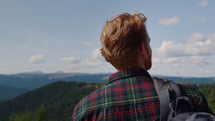 Male hiker standing on top of mountain. Redhead man looking summer landscape