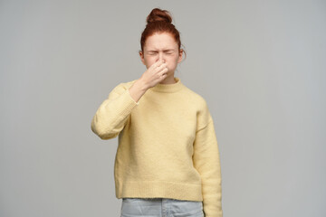 Portrait of sneezing, adult girl with ginger hair bun. Wearing yellow sweater. Squint her closed...