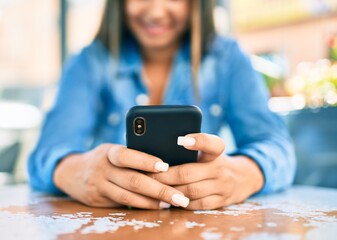 Young latin woman smiling happy using smartphone at coffee shop terrace.