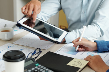 Close-up image of businessman pointing at screen of tablet computer when showing product presentation he created to colleague