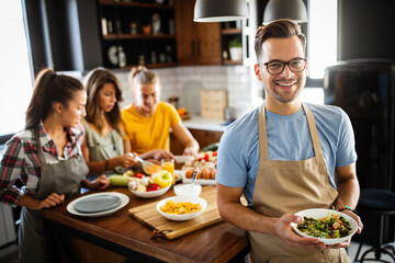 Group of happy friends laughing and talking while preparing meals in kitchen