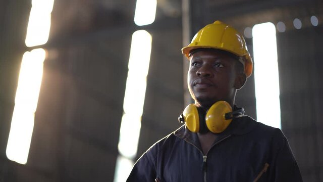portrait of african american heavy industry worker wearing hard hat and yellow ear muffs standing confident  holding  wrench tools in Large Industrial Factory. young  black engineer