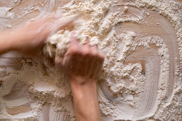 Hands knead the dough, on a wooden table. Photo in motion, blur. Top view.