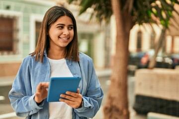 Young latin girl smiling happy using touchpad at the city.