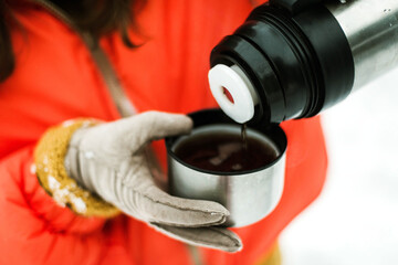 Woman in orange jacket drinking hot tea outdoors in winter.