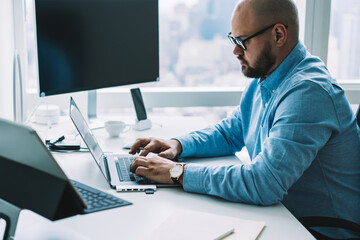 Crop concentrated manager typing on laptop in modern office