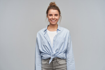 Happy woman, positive blond girl with hair bun. Wearing blue striped knotted shirt. Standing...