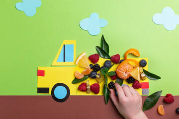 Kids food art concept: paper craft truck with berries and fruits on green concept top view, flat lay