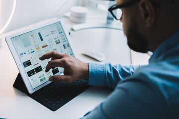 Crops serious man working on tablet placed on keyboard in stylish office