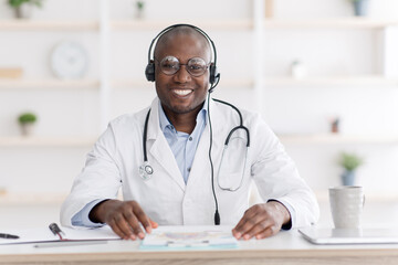 Healthcare and medicine concept. Cheerful african american doctor smiling to camera, sitting at his workplace in office