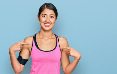 Fototapeta na wymiar Beautiful asian young sport woman wearing sportswear and arm band looking confident with smile on face, pointing oneself with fingers proud and happy.