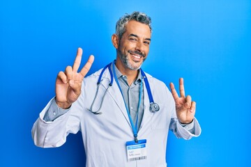 Middle age grey-haired man wearing doctor uniform and stethoscope smiling looking to the camera...