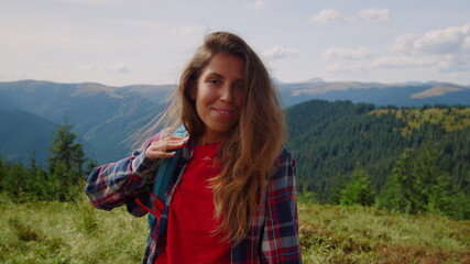 Woman wearing backpack in mountains. Positive hipster waving hand at camera