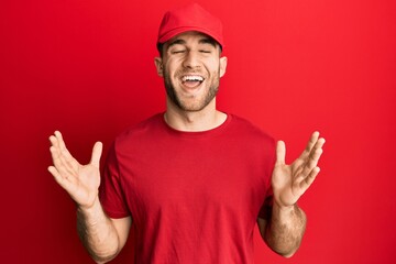 Young caucasian man wearing delivery uniform and cap celebrating mad and crazy for success with arms raised and closed eyes screaming excited. winner concept