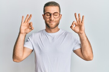 Young caucasian man wearing casual clothes and glasses relax and smiling with eyes closed doing meditation gesture with fingers. yoga concept.