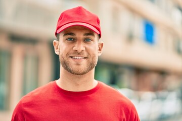 Young caucasian deliveryman smiling happy standing at the city.