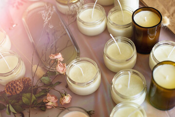 Soy Candles poured into recycled bottles and jars. Many soy wax candles together on store or workshop background. . Ecological and vegan business. - obrazy, fototapety, plakaty