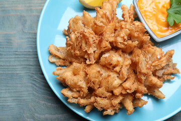 Fried blooming onion with dipping sauce served on blue wooden table, top view