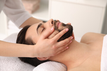 Obraz na płótnie Canvas Young man receiving facial massage in beauty salon