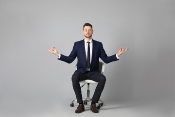 Fototapeta na wymiar Handsome businessman meditating in office chair on grey background