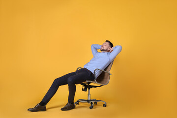 Handsome man relaxing in office chair on yellow background
