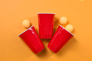 Plastic cups and balls for beer pong on orange background, flat lay
