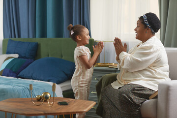 Side view portrait of cute African-American girl having fun with grandmother in cozy home setting,...