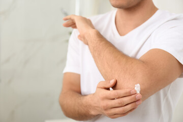 Man applying cream onto elbow indoors, closeup